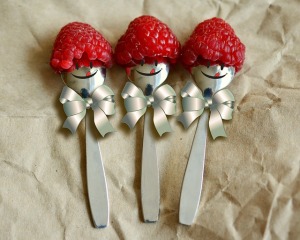 Three teaspoons lying side by side, each with a raspberry hat, a face painted on, and a little silver bow